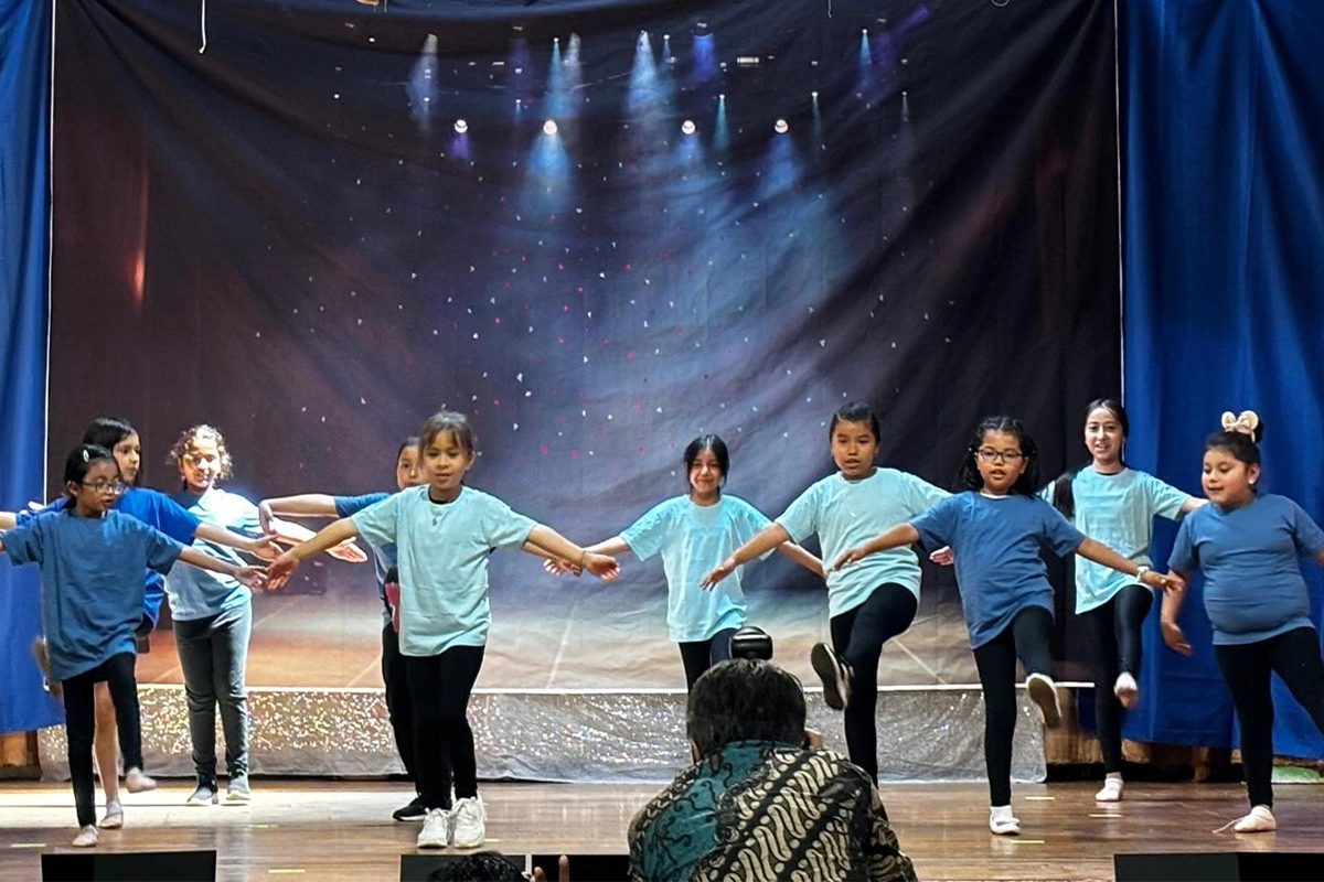 Grupo de niños presentando una obra de danza en un escenario iluminado.